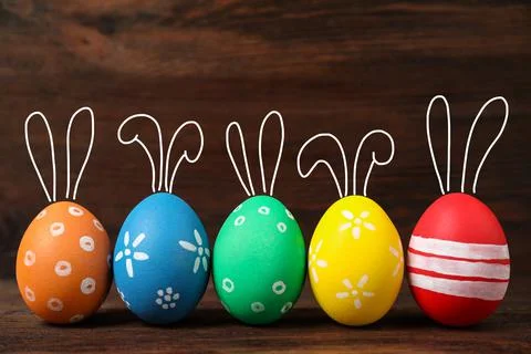 Bright Easter eggs with cute bunny ears on wooden background Foto stock