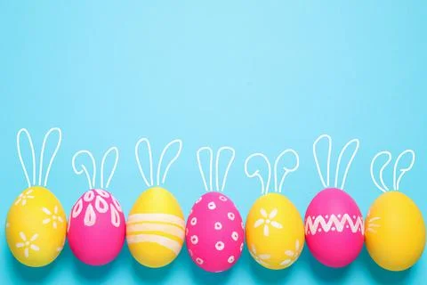Bright Easter eggs with cute bunny ears and space for text on light blue back Fotos de archivo
