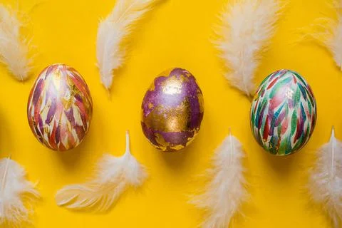 Bright Easter eggs decorated with golden foil, white feathers on yellow Stock Photos