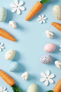 Bright Easter frame with orange carrots, white bunnies, colored eggs and flow Stock Photos