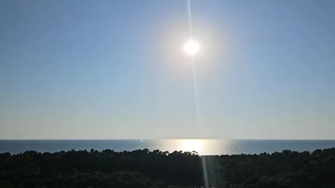 Bright evening sun reflects across the calm Black Sea beyond a dark forested Stock Footage 344886553