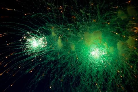 A bright firework with a green glowing center with orange sparks flying towards Stock Photos