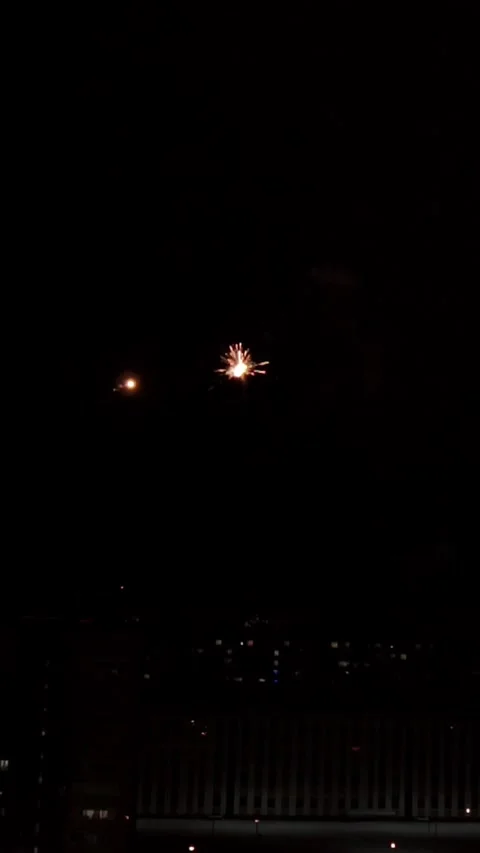 Bright fireworks explode in dark night sky above distant urban building during Stock-Footage 348026526