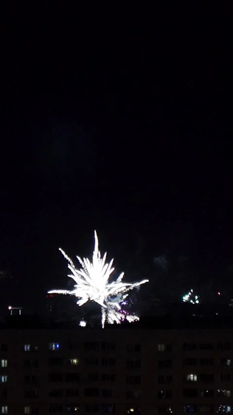 Bright fireworks explode in night sky above apartment building silhouette Video stock 346641115