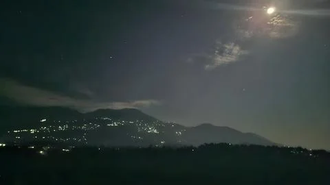 Bright full moon illuminates the dark night sky above hazy mountain ranges d Stock Photos