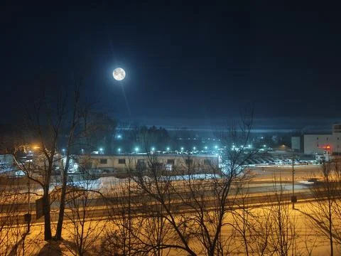A bright full moon illuminates a sleeping winter city Stock Photos