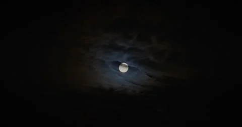 Bright full moon partially covered by moving dark clouds at night, creating a m Stock Footage 341142543