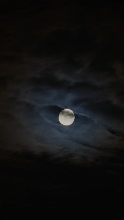 Bright full moon partially covered by moving dark clouds at night, creating a Stock Footage 341362509