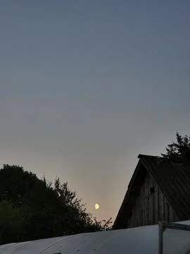 Bright full moon in twilight sky above countryside house roof Stock Photos