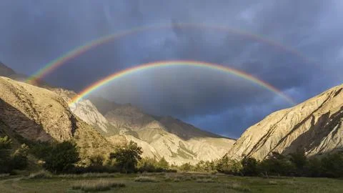Bright full rainbow on the background of storm cloud over mountain range and Stock Photos