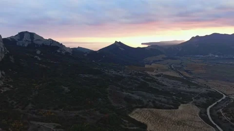 Bright glow of sunset under a cloudy sky over a mountain range and vineyards in Stock Footage 151145411