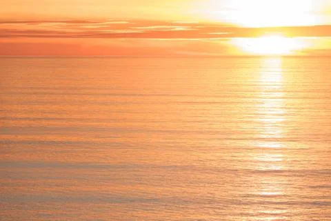 Bright golden dramatic sunset sun reflecting orange, gold, off calm ocean Stock Photos