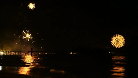 Bright golden fireworks explode in the night sky above the surface of the sea Vidéo 86715871