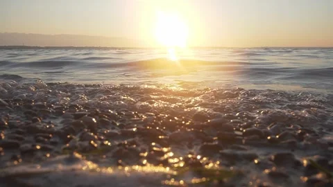 Bright golden sun shining over calm water and pebble shore Stock Footage 337306697