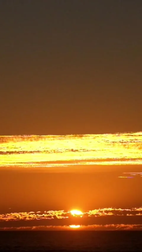 Bright golden sun slowly sinking below the tranquil ocean horizon, casting a Stock Footage 344816230