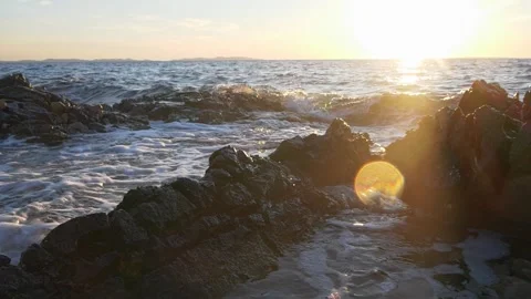 Bright golden sunset glowing over rocky ocean coastal water waves Stock Footage 337409370