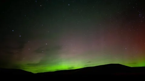 Bright green and red aurora flash in a star filled sky above rolling hills.  Stock Footage 251055491