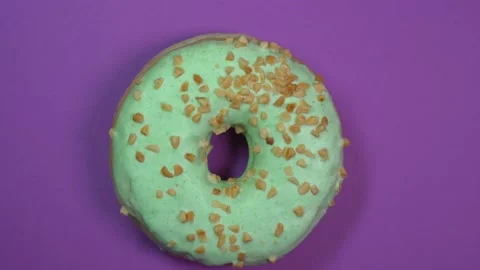Bright green glazed donut with nuts close-up, macro shot, spinning on a purple Stock Footage 89729195