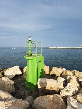 Bright green navigation light beacon on rocky harbor pier with calm blue se.. Stock Photos