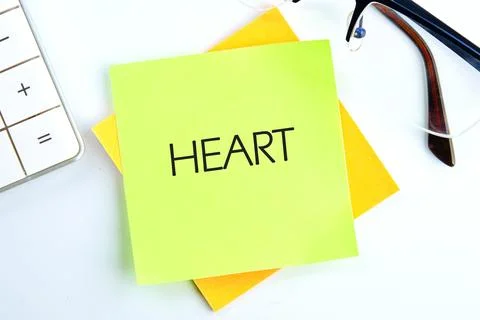 A bright green sticky note displaying the word heart is placed on a desk, acc Stock Photos