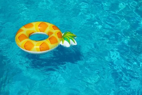 Bright inflatable pineapple ring floating in swimming pool on sunny day. Spac 스톡 사진