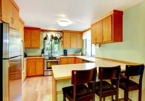 Bright kitchen with light brown cabinets, steel appliances and old wooden sto Stock Photos