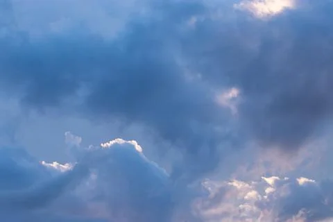 Bright light and dark clouds color the sky gray blue and purple during sunset Stock Photos