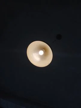 Bright Light Bulb Glowing Inside a Modern Pendant Lamp on a Dark Ceiling Stock-Fotos