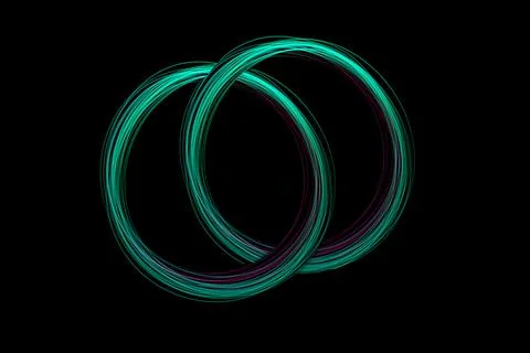 Bright light circles intertwine in an artistic display, showcasing flowing .. 스톡 사진