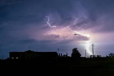 Bright lightning bolt is hitting the ground near a ranch. Stock Photos
