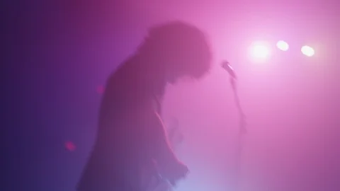 Bright lights shine on the back of a man as he plays guitar on stage Stock Footage 127144424