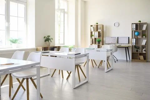 Bright modern classroom interior with white desks, chairs, shelves and computer Stock Photos