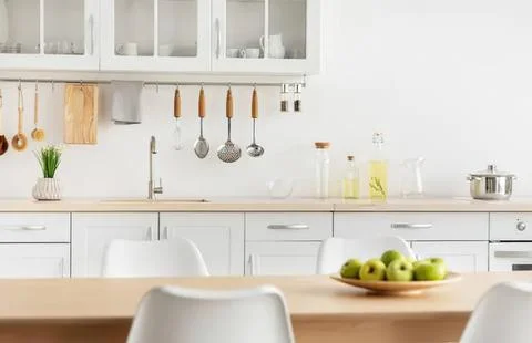 Bright modern kitchen with white cabinets and wooden table Stock Photos