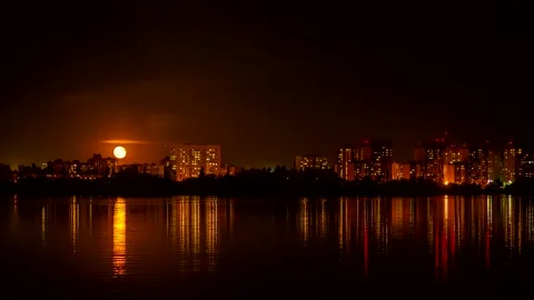 A bright moon rises above the sleeping night city of timelapse. Reflections Stock Footage 132609613