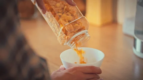 In bright morning kitchen womans hands scoop measured corn flakes into bowl Stock Footage 335125083