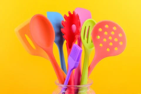 Bright multi colored kitchen utensils on yellow background Stock Photos