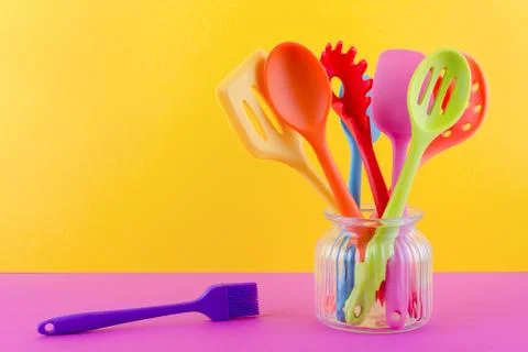 Bright multi colored kitchen utensils on yellow background with copy space Stock Photos