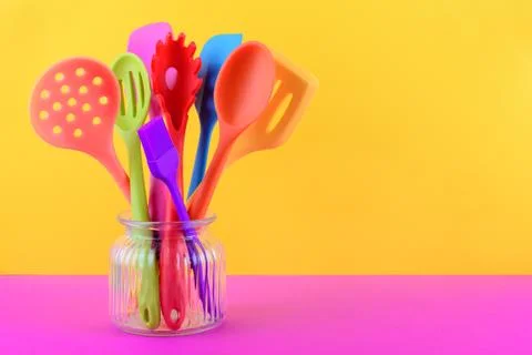 Bright multi colored kitchen utensils on yellow and purple background with copy Stock Photos