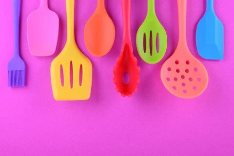 Bright multi colored kitchen utensils on purple background with copy space Stock Photos