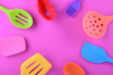 Bright multi colored kitchen utensils on purple background with copy space Stock Photos