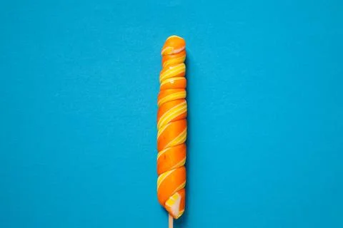 Bright multi-colored spiral-shaped lollipop on a blue background. Space copy. Stock Photos