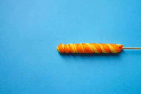 Bright multi-colored spiral-shaped lollipop on a blue background. Space copy. Stock Photos