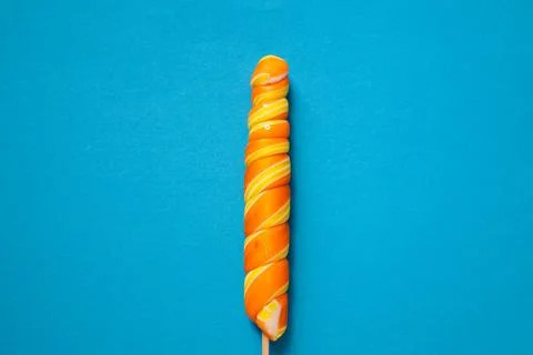 Bright multi-colored spiral-shaped lollipop on a blue background. Space copy. Stock Photos