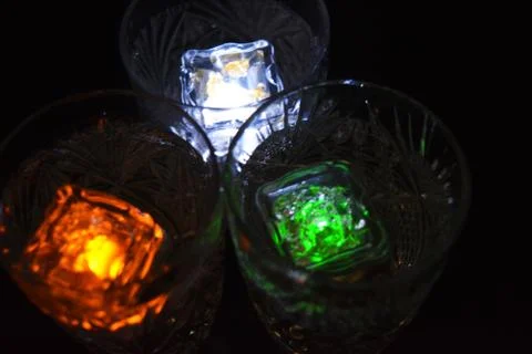 Bright multicolor doidic glowing ice cubes float in the drink. Stock Photos