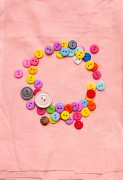 Bright multicolored buttons in the shape of a circle on a light pink fabric Stock Photos