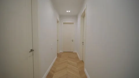  A bright, narrow corridor with a herringbone pattern wood floor and neutral-ton Stock Footage 269027870
