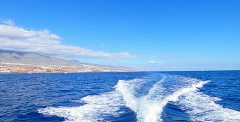 Bright ocean panorama with white waves behind moving boat near Tenerife islan 库存照片