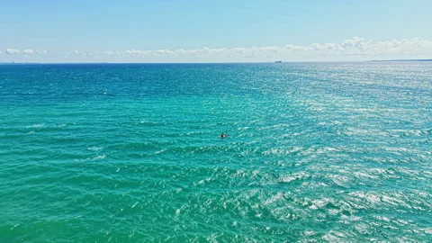 Bright ocean waves and clear sky over the water near a beach with distant boats Stock Footage 344211072