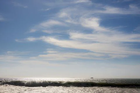 Bright ocean waves crash under a vast blue sky with wispy clouds and distan.. Fotos de archivo