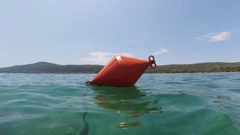 Bright orange buoy floating in clear turquoise sea near a forested coastline Stock Footage 313800805
